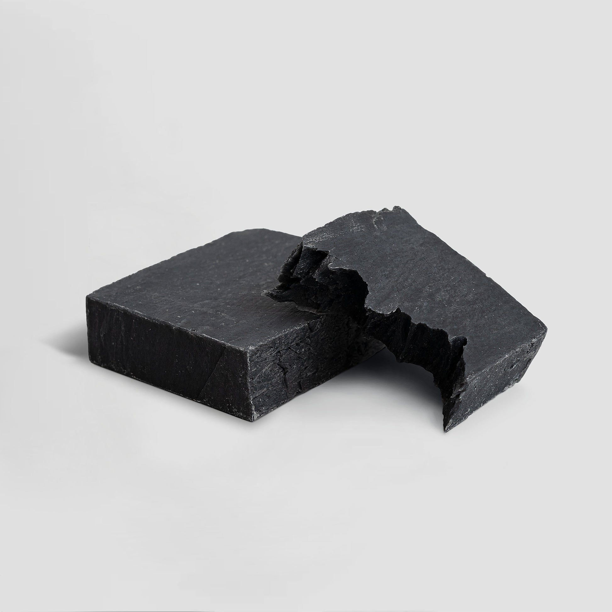 Two pieces of black soap on a light gray background